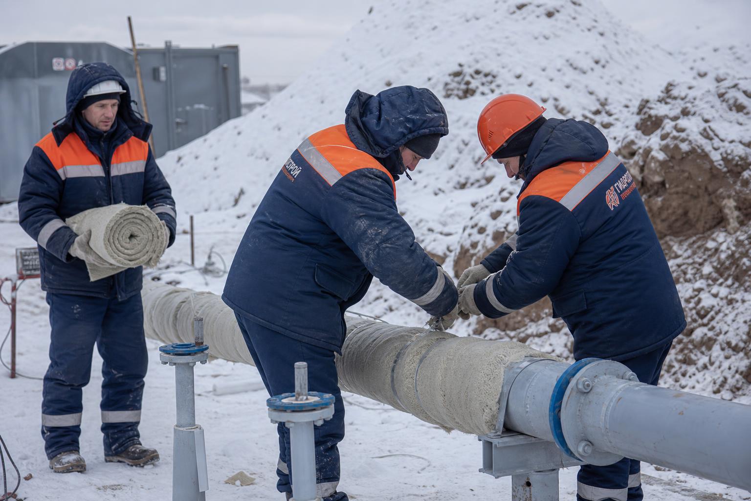 Рабочие утепляют трубопроводы иглофильтровой системы на зимней строительной площадке в России