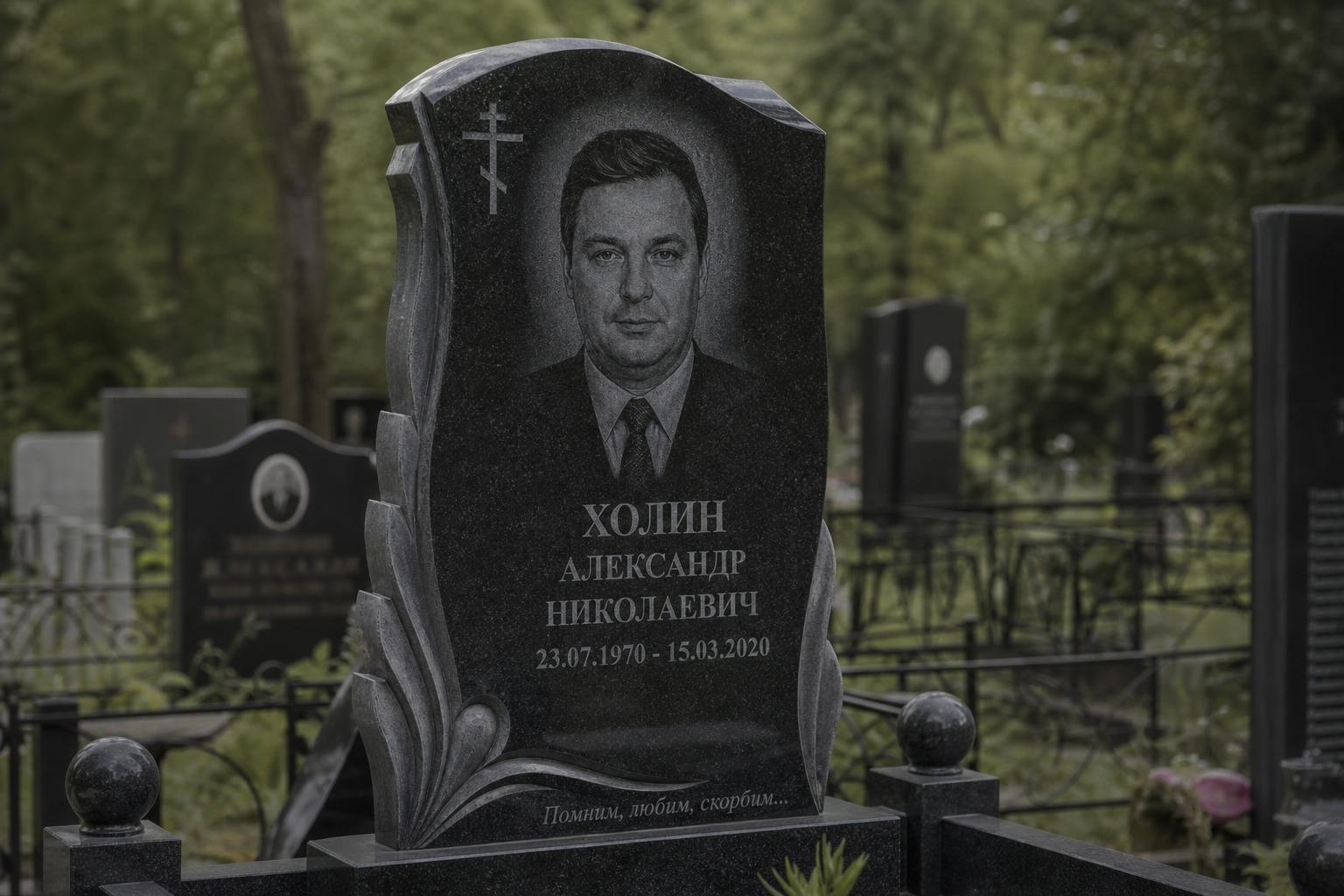 Гранитный памятник с выгравированными ФИО, датами и эпитафией на фоне кладбища